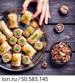Hand holding Turkish baklava near walnuts on wooden background  . Стоковое фото, агентство Ingram Publishing / Фотобанк Лори