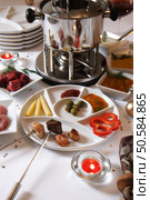 Festlich eingedeckter Tisch mit Fleischfondue. Weisse Tischdecke mit weissem Geschirr und weihnachtlicher Deko und Kerzen. Стоковое фото, агентство Ingram Publishing / Фотобанк Лори