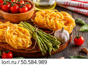 Products for cooking - fresh asparagus, pasta, tomatoes, garlic, olive oil on the old wooden background. Стоковое фото, агентство Ingram Publishing / Фотобанк Лори