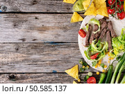 Food background with nachos chips and ingredients for making tartilla. Onion, tomatoes, chili peppers, beef, tortillas and corn with deeps over old wooden surface. Flat lay with copy space. Food background with tortilla ingredients. Стоковое фото, агентство Ingram Publishing / Фотобанк Лори