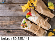 Mexican style dinner. Two papered tortillas burrito with beef and vegetables served with nachos chips and guacomole sauce over old wooden background. Flat lay. Tortillas and nachos. Стоковое фото, агентство Ingram Publishing / Фотобанк Лори