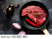 One raw beef steak with spices, onions and chili on dark slate or concrete background. Top view. Стоковое фото, агентство Ingram Publishing / Фотобанк Лори