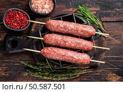 Raw kofta or lula kebabs skewers on a grill with herbs. Dark wooden background. Top view. Стоковое фото, агентство Ingram Publishing / Фотобанк Лори
