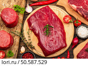 Set of various steaks with traditional spices and herbs. Fresh raw meat cuts includes ribeye, eye round, flank and striploin steaks. Old wooden background, flat lay, top view. Стоковое фото, агентство Ingram Publishing / Фотобанк Лори