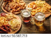 a variety of snacks for beer. Cheese, sausages, chips, snacks, potatoes, rustic, sauce the beer mugs on wooden background. snacks to beer on wooden background top view. Стоковое фото, агентство Ingram Publishing / Фотобанк Лори