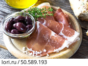 Thin slices of prosciutto with  olives on wooden background. Стоковое фото, агентство Ingram Publishing / Фотобанк Лори