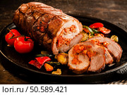 Gourmet Food Close Up of Roast Pork Roll Stuffed with Tomatoes and Grilled Vegetables and Served on Sizzling Cast Iron Pan and Rustic Wooden Table. Roast Pork Roll Stuffed with Grilled Vegetables. Стоковое фото, агентство Ingram Publishing / Фотобанк Лори