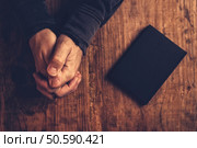 Christian man praying with hands crossed and Holy Bible by his side on wooden desk in church, top view. Стоковое фото, агентство Ingram Publishing / Фотобанк Лори