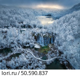 Aerial drone view of frozen lake, waterfall and snowy forest at sunset. Winter fairytale in Plitvice Lakes, Croatia. Top view of white snow-covered trees, waterfall, trails, fog, cloudy sky. Nature. Стоковое фото, агентство Ingram Publishing / Фотобанк Лори