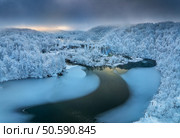 Aerial drone view of frozen lake, waterfall and snowy forest at sunset. Winter fairytale in Plitvice Lakes, Croatia. Top view of white snow-covered trees, waterfall, trails, fog, cloudy sky. Nature. Стоковое фото, агентство Ingram Publishing / Фотобанк Лори
