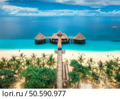 Aerial view of bungalow, white sandy beach, ocean on summer sunny day. Restaurant on the sea. Top drone view of wooden hotel, azure water, palms, sky with clouds. Luxury resort in Kendwa, Zanzibar. Стоковое фото, агентство Ingram Publishing / Фотобанк Лори