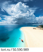 Aerial view of tropical sea coast, empty white sandy beach and boat on summer sunny day. Travel in Kendwa, Zanzibar island. Landscape with boat, clear blue water, dramatic sky, clouds, palms. Top view. Стоковое фото, агентство Ingram Publishing / Фотобанк Лори