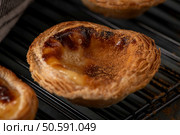 Portuguese custard tart with a flaky, golden-brown crust and a creamy, caramelized filling, cooling on a black wire rack. Стоковое фото, агентство Ingram Publishing / Фотобанк Лори