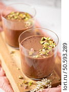 Two glasses of chocolate mousse topped with chopped pistachios a delicious sweet dessert still life. Стоковое AI-изображение, агентство Ingram Publishing / Фотобанк Лори