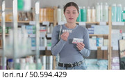 Careful young woman holding paracetamol with box making choice in drugstore. Стоковое видео, видеограф Яков Филимонов / Фотобанк Лори