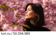 Woman enjoying cherry blossoms in full bloom during spring amid vibrant pink flowers on a sunny day. Стоковое AI-изображение, AI-художник Сергей Толмачёв / Фотобанк Лори