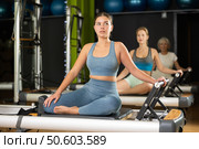 Girl sitting on foldable bed reformer performs exercises, strengthening body and muscles. Стоковое фото, фотограф Яков Филимонов / Фотобанк Лори