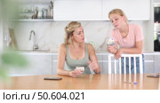 Interested teenage girl asking for pocket money from mother sitting at table in kitchen, counting received salary. Стоковое видео, видеограф Яков Филимонов / Фотобанк Лори