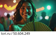 A woman with a green fan smiling in a dimly lit venue, fairy lights creating bokeh effects in background, music laser show on background. Стоковое AI-видео, аниматор Sergey Grishin / Фотобанк Лори