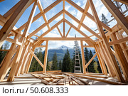 Wooden roof frame of a new house being constructed with mountain view. Стоковое AI-изображение, AI-художник Иван Рябоконь / Фотобанк Лори