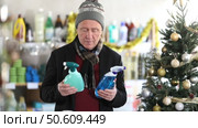 In Christmas atmosphere, senior man studies label and choose kitchen cleaner spray. Стоковое видео, видеограф Яков Филимонов / Фотобанк Лори