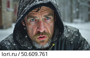 A close-up portrait of a desperate, homeless man with a beard and blue eyes in a hooded jacket, looking at the camera during a winter snowstorm. Стоковое AI-видео, аниматор Sergey Grishin / Фотобанк Лори