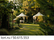 Luxurious gazebos providing shade in lush green garden during sunset. Стоковое AI-изображение, AI-художник Иван Рябоконь / Фотобанк Лори