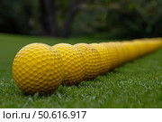 Row of yellow golf balls lying on green grass of driving range. Стоковое AI-изображение, AI-художник Иван Рябоконь / Фотобанк Лори