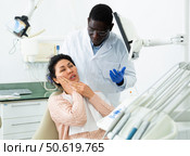 Woman patient who came to an appointment with a male dentist is sitting in a dental chair in clinic office, showing which side of her tooth aches. Стоковое фото, фотограф Яков Филимонов / Фотобанк Лори