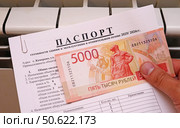 Мужская рука держит паспорт готовности здания к эксплуатации в отопительном сезоне и российские деньги на фоне батареи отопления в квартире. Стоковое фото, фотограф Цибаев Алексей / Фотобанк Лори