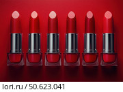 Row of passion red lipsticks displayed against a vibrant red background. Beauty industry and fashion concept. Copy space. Advertisement for makeup artists. Стоковое AI-изображение, AI-художник Ирина Михайличенко / Фотобанк Лори