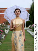 Elegant woman holding white parasol in garden setting. Стоковое AI-изображение, AI-художник Юрий Поздников / Фотобанк Лори