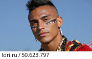 Indigenous man wearing traditional makeup and clothing posing under blue sky. Стоковое AI-изображение, AI-художник Юрий Поздников / Фотобанк Лори