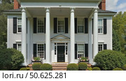 Front side of typical american porch colonial house with white traditional columns and pillars, beautiful garden in the back and forest behind backyard on background. Стоковое AI-видео, аниматор Sergey Grishin / Фотобанк Лори