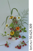 Vertical video of the summer rural composition with a ripe tasty strawberries and the bouquet of seasonal marigold, daisy flowers and berries on the kenzan holder in a low vase on a white background. Стоковое видео, видеограф Виктория Катьянова / Фотобанк Лори