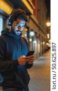 Hispanic young attractive man stands in dark street in front of shop, changes songs and tracks on smartphone, listens to music in wireless headphones. Hipster wearing casual dress. Стоковое AI-видео, аниматор Sergey Grishin / Фотобанк Лори