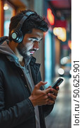 Hispanic young attractive man stands in dark street in front of shop, changes songs and tracks on smartphone, listens to music in wireless headphones. Hipster wearing casual dress. Стоковое AI-видео, аниматор Sergey Grishin / Фотобанк Лори