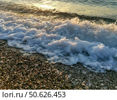 Waves crashing on pebbled beach at sunset, creating foam and shimmering reflections on water. Стоковое фото, фотограф Наталья Семкина / Фотобанк Лори