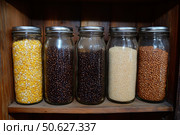 Colorful jars filled with groceries, various grains, spices on wooden shelf. Neatly arranged collection of glass jars. Home storage. Close-up of various food. Storing in a kitchen. Bulk staple foods. Стоковое AI-изображение, AI-художник Марина Демидюк / Фотобанк Лори