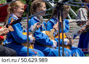 Каменномостский, Россия - Июнь 28, 2025: Девочки из детского казачьего ансамбля выступают на сцене играя на балалайках на 34 фестивале казачьей культуры в Адыгее. Редакционное фото, фотограф Андрей С / Фотобанк Лори