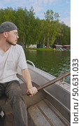 A young fisherman, with a beard, is rowing a boat on the river in the summer. Стоковое видео, видеограф Strunov David / Фотобанк Лори