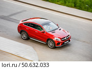 Red luxury SUV Mercedes GLE speeds down an urban street, showcasing its sleek design and power. The dynamic shot captures the motion and elegance of the high-performance vehicle and city atmosphere. Редакционное фото, фотограф Константин Григорьев / Фотобанк Лори