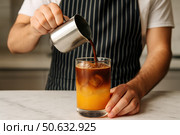 Бариста наливает холодный кофе в стакан с апельсиновым соком и льдом на белом столе. Стоковое AI-изображение, AI-художник Башкирова Анна / Фотобанк Лори