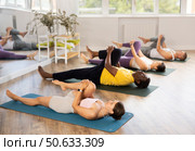 Young woman performing Eka Pada Apanasana in yoga class. Стоковое фото, фотограф Яков Филимонов / Фотобанк Лори