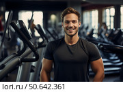 Handsome personal trainer smiling in modern fitness center with elliptical machines. Стоковое AI-изображение, AI-художник Иван Рябоконь / Фотобанк Лори