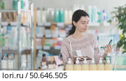 Female shopper in autumn clothes chooses best cosmetic in supermarket. Стоковое видео, видеограф Яков Филимонов / Фотобанк Лори