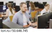 Man student of computer courses looks at monitor screen, types on keyboard and does work. Стоковое видео, видеограф Яков Филимонов / Фотобанк Лори