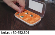 Hand placing light-yellow vitamin D capsules into a weekly pill organizer for medication management. Стоковое видео, видеограф Татьяна Степанищева / Фотобанк Лори
