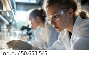Young scientists conduct experiments in a laboratory, focusing on research and observations during the day. Стоковое AI-изображение, AI-художник Сергей Толмачёв / Фотобанк Лори
