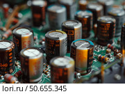 Electrolytic capacitors populating a green circuit board. Стоковое AI-изображение, AI-художник Иван Рябоконь / Фотобанк Лори
